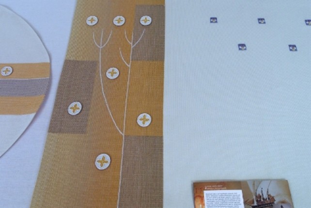 Valkoinen alttarivaate ja kasukka valmiina ompelimon pöydällä. Tekstiilien symboleina keltamon ja keto-orvokin kukat sekä pääskynen. Keltamoa kutsutaan myös pääskysyrtiksi.